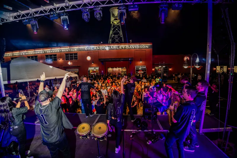 Band performing on stage to a packed crowd under concert lighting outside Orlando Harley-Davidson at night