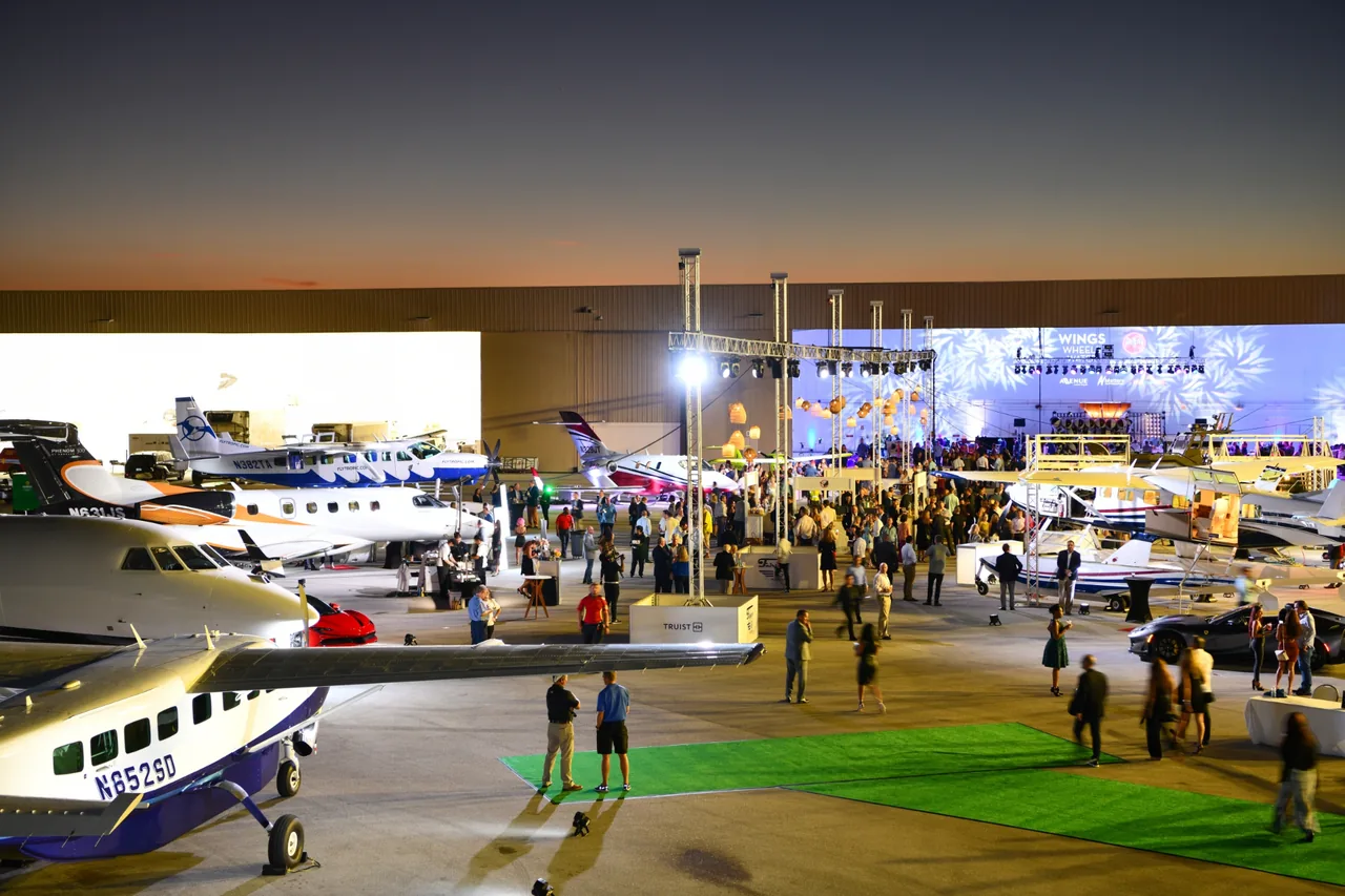 Evening event on an airfield tarmac with private aircraft, guests, and a lit stage