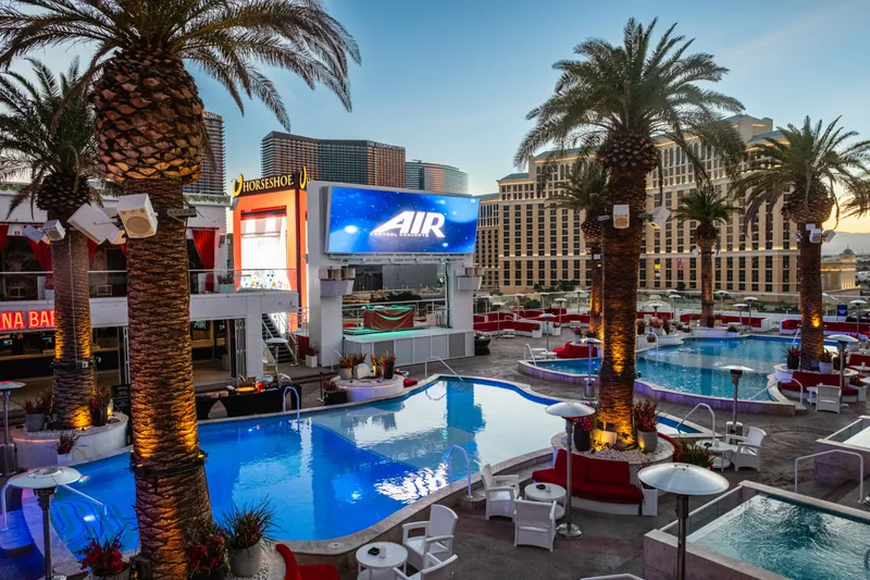 Sunset cocktail setup on a Las Vegas Strip rooftop pool deck with cabanas, palms and an LED stage
